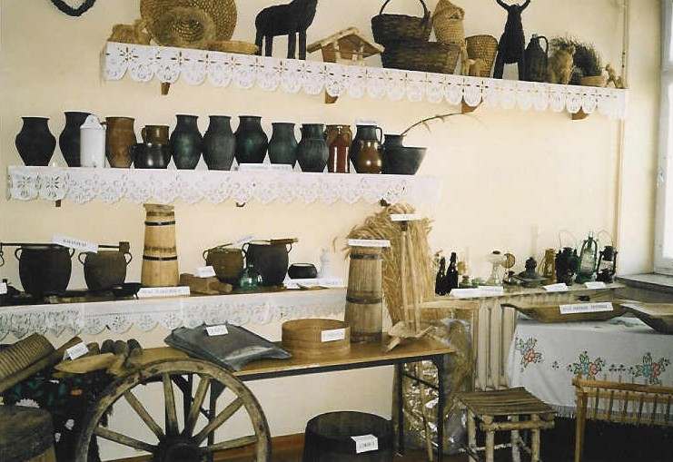Muzealne eksponaty: stare żelazka, naczynia do wyrobu ciasta na chleb, stare koło od wozu, gwiazda  kolędników.